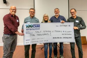 Stella Weinert stands in the middle of representatives from 100 Men Who Care Salt Spring Island. They hold a giant cheque made out to Salt Spring Literacy for the amount of $10,000